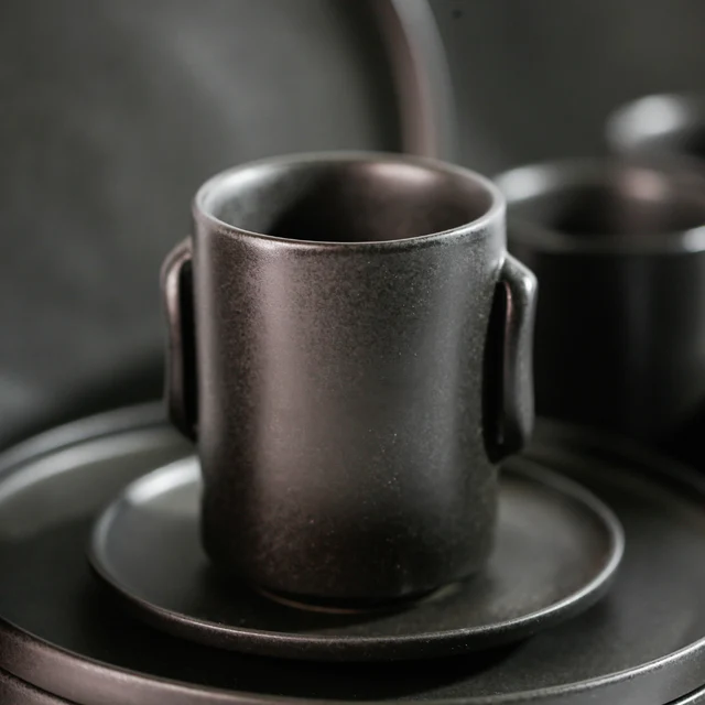 Dark ANELLO cylindrical cup with two side tabs, photographed on a saucer