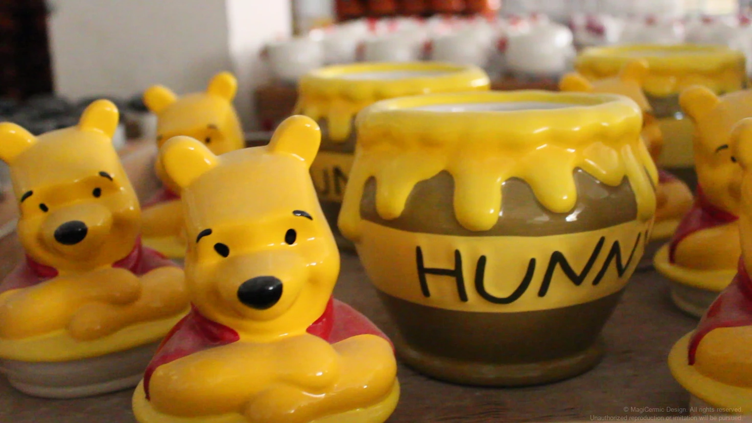 Winnie the Pooh figures displayed beside a yellow ceramic hunny jar and related mugs