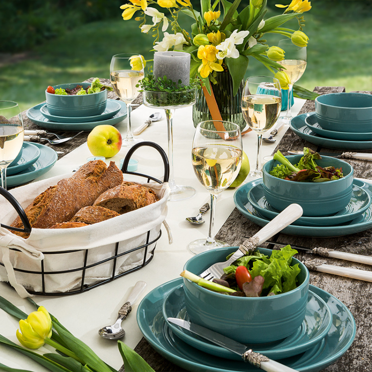 Teal plates and bowls set on an outdoor dining table with food and flowers